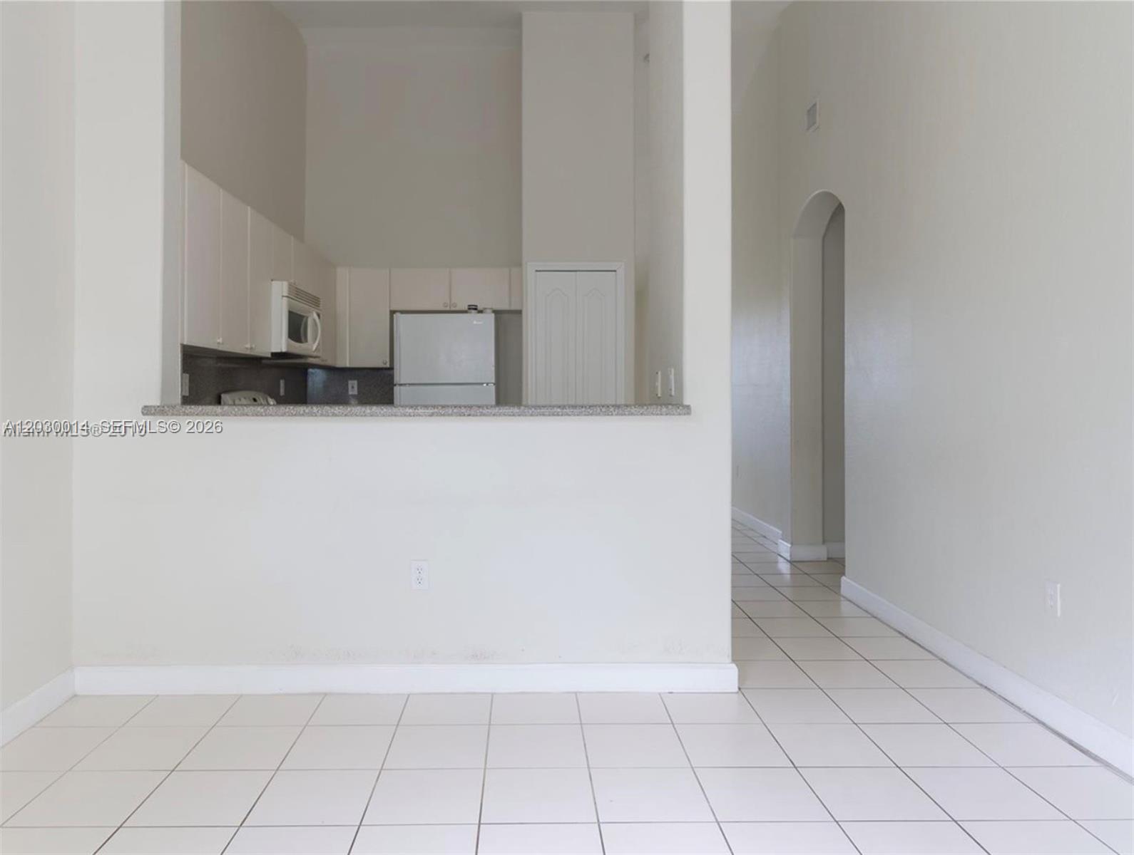 A kitchen with white cabinets and a breakfast bar overlooks a tiled living area — 2755 SE 16th Ave # 202, Homestead FL 33035, HOMESTEAD, FL