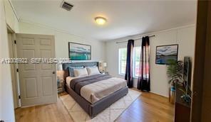 A bedroom features a queen bed, light wood flooring, two windows with curtains, and wall art — 1047 Mayford Lake Rd, Moore Haven FL 33471, MOORE HAVEN, FL