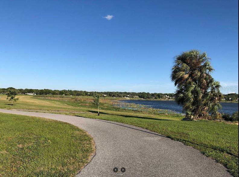 A paved walking path winds through a grassy park toward a lake and palm tree — N/A, LAKE WALES, FL