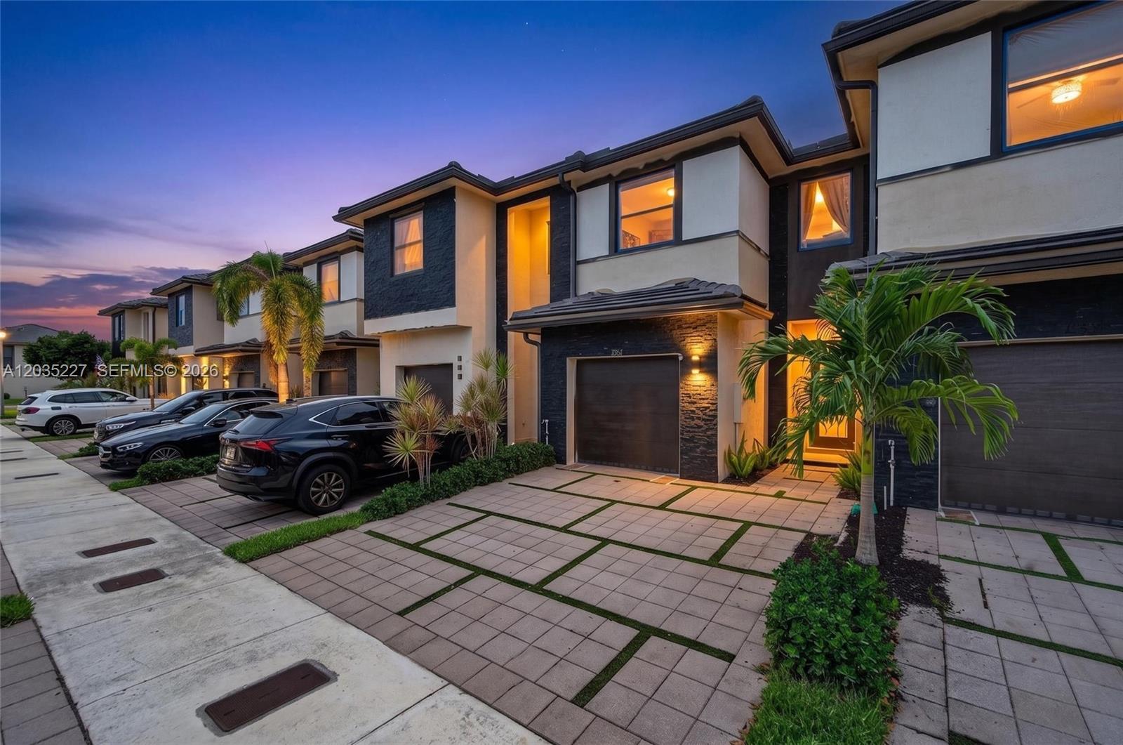 A row of modern townhouses with paved driveways, stone accents, and palm trees at dusk — 15841 NW 91st Ct, Miami Lakes FL 33018, MIAMI LAKES, FL