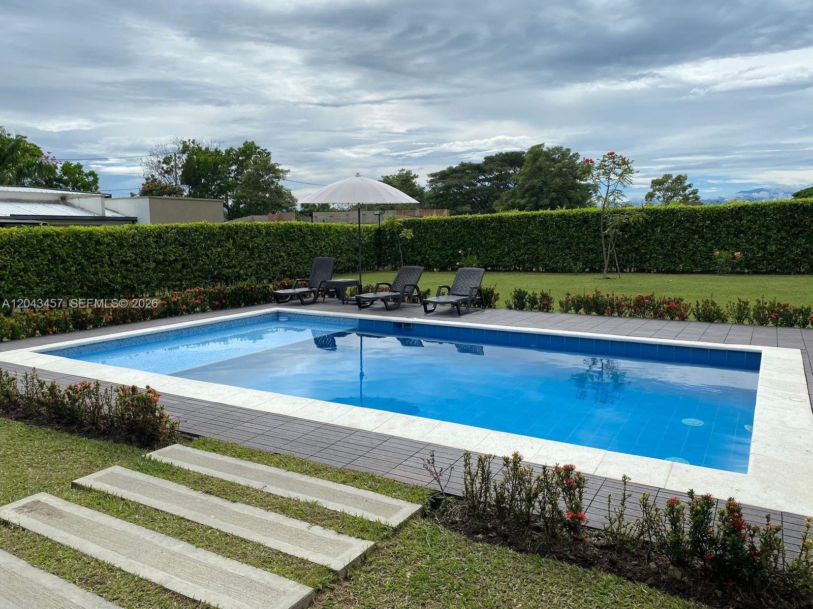 A rectangular swimming pool with a patio, lounge chairs, and an umbrella in a backyard — 0 GINEBRA VALLE COL, FL, FL