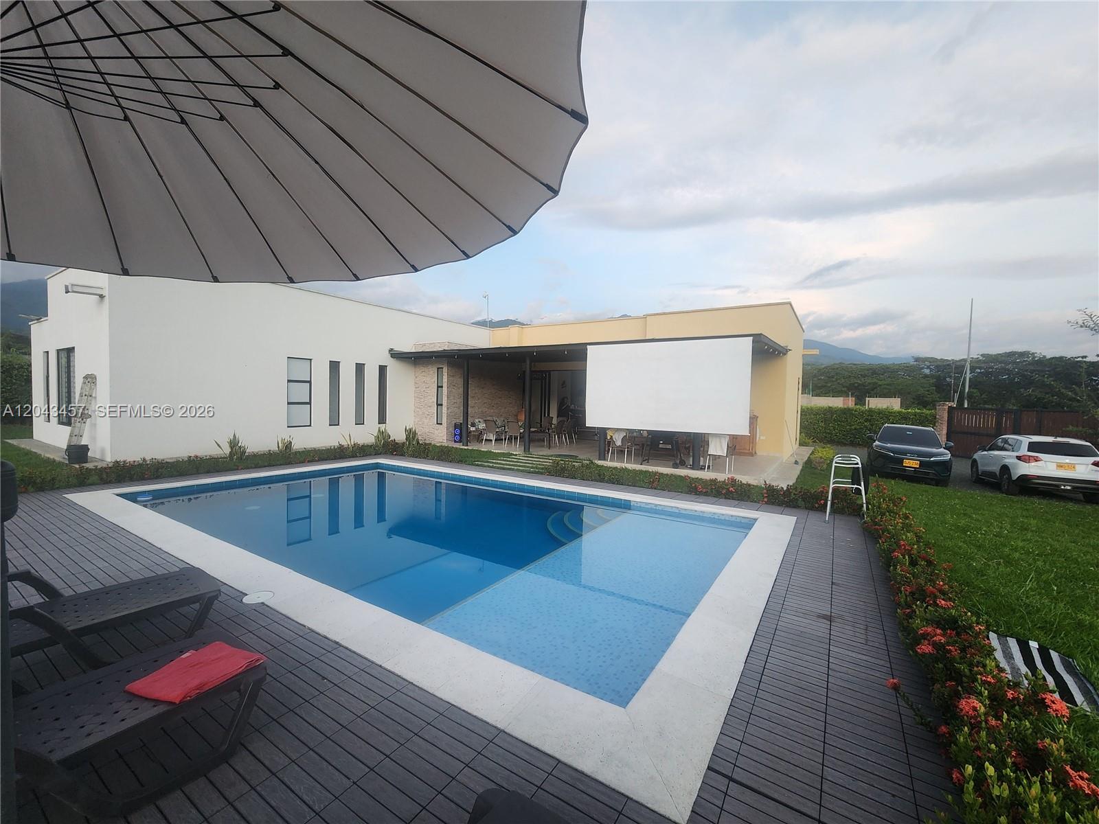 A rectangular swimming pool sits on a wooden deck next to a modern house — 0 GINEBRA VALLE COL, FL, FL