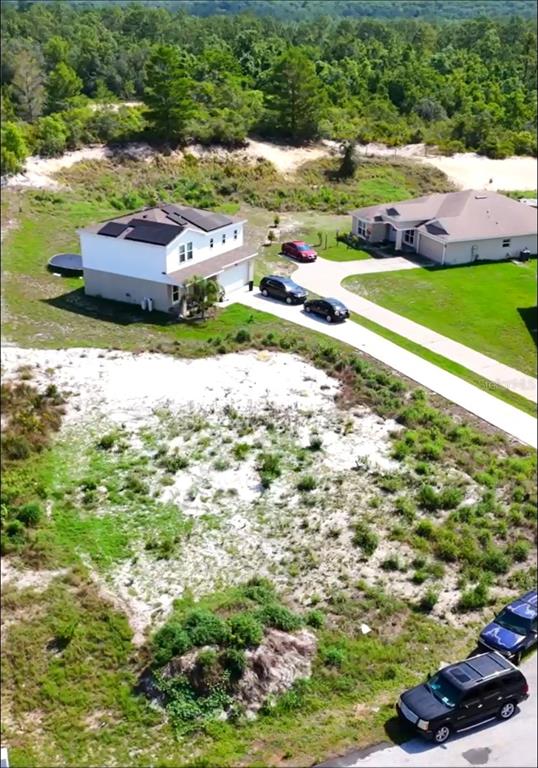 An aerial view shows a two-story house with solar panels next to a vacant lot — 17 LARCH LANE, KISSIMMEE, FL
