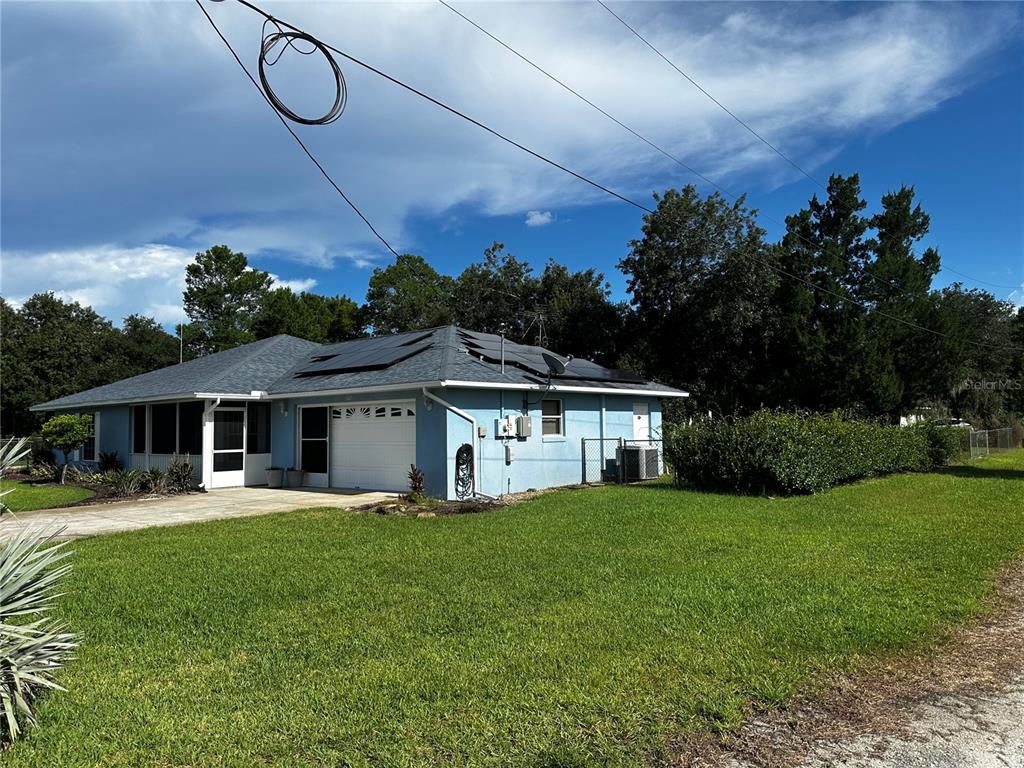 A light blue single-story house with a white garage door and roof-mounted solar panels — 5005 GRAND CONCOURSE, SEBRING, FL