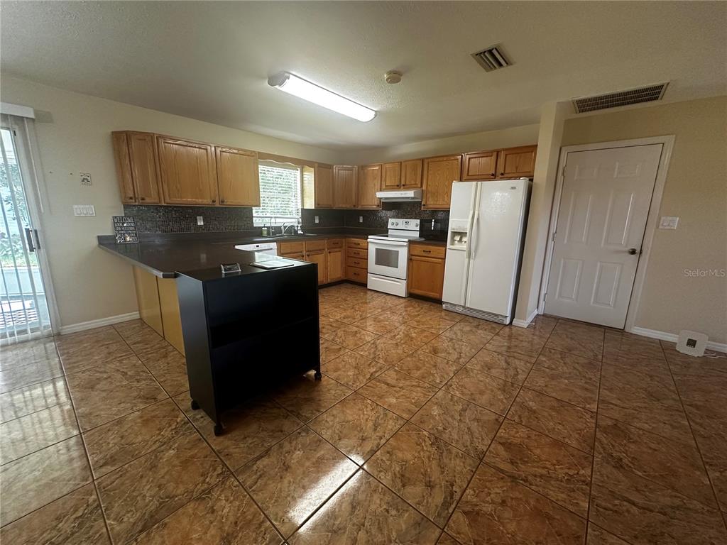 A kitchen features wood cabinets, dark countertops, white appliances, and brown tile flooring — 5005 GRAND CONCOURSE, SEBRING, FL