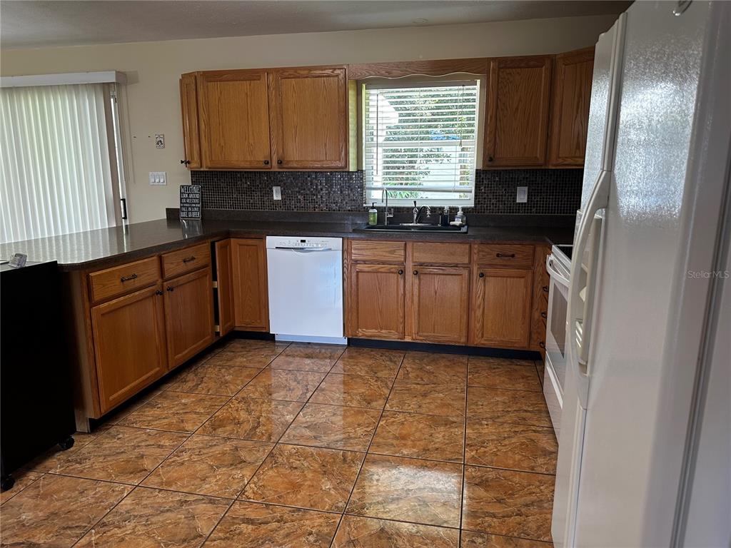 A kitchen features wood cabinets, dark countertops, a tiled backsplash, and brown patterned floor tiles — 5005 GRAND CONCOURSE, SEBRING, FL