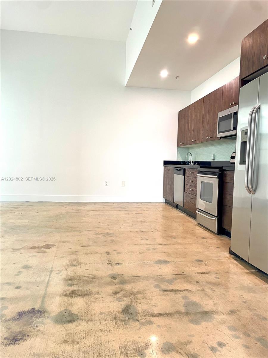 A kitchen area features a stainless steel refrigerator, stacked laundry unit, and unfinished concrete flooring — 935 Euclid Ave # 6, Miami Beach FL 33139, MIAMI BEACH, FL