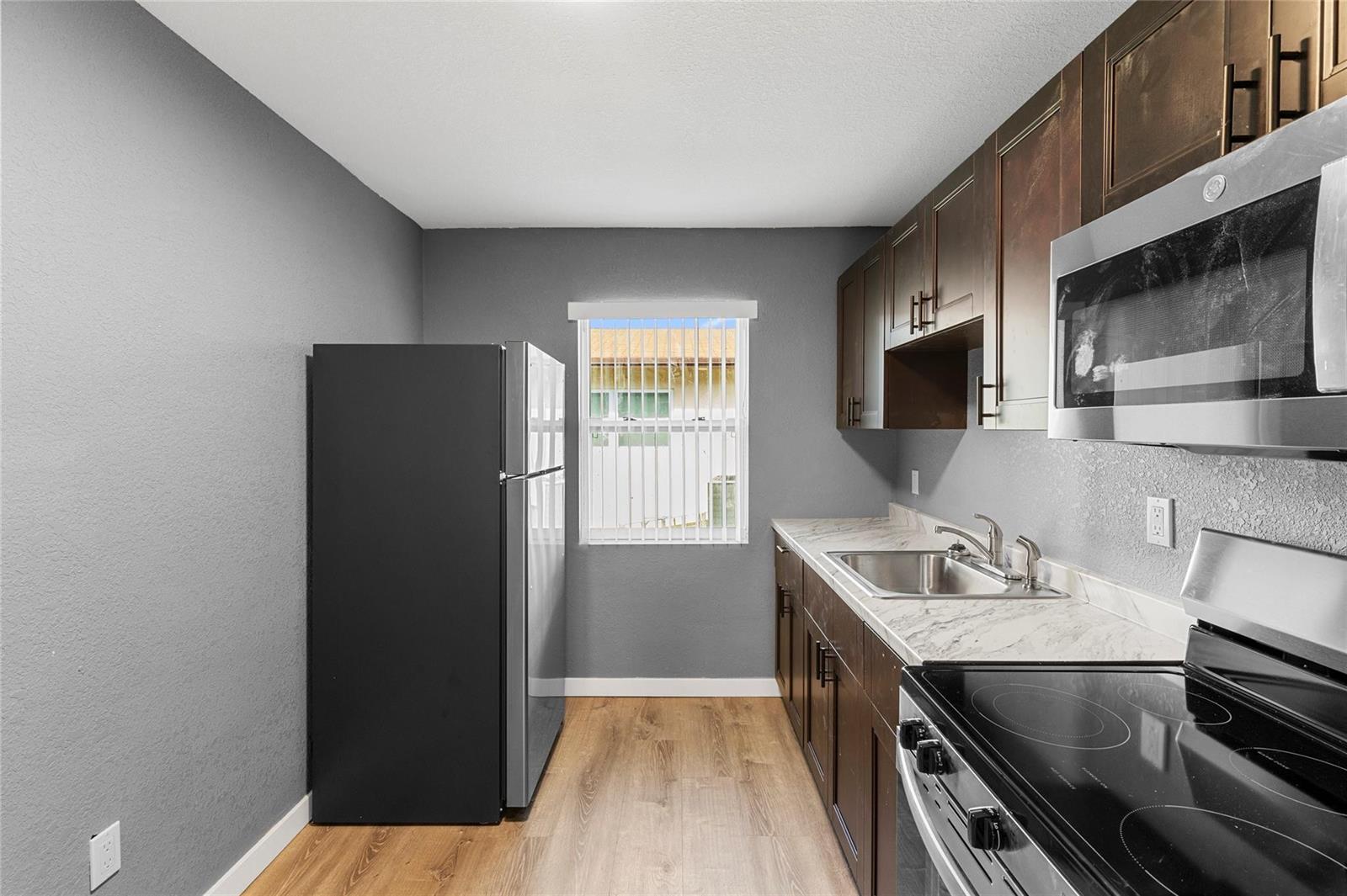 A galley kitchen features dark wood cabinets, stainless steel appliances, and gray walls — 229 NW 12th Court, Pompano Beach FL 33060, POMPANO BEACH, FL