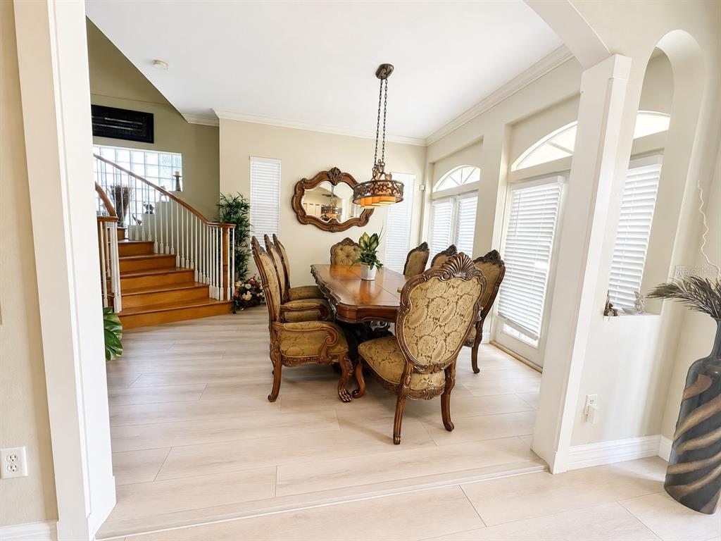 A dining room features a wooden table, upholstered chairs, a chandelier, and a staircase nearby — 3517 HAINES ROAD N, ST PETERSBURG, FL