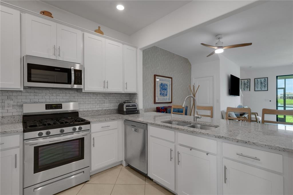 A kitchen with white cabinets, stainless steel appliances, granite countertops, and a tile backsplash — 15227 SUNNY DAY DRIVE, BRADENTON, FL