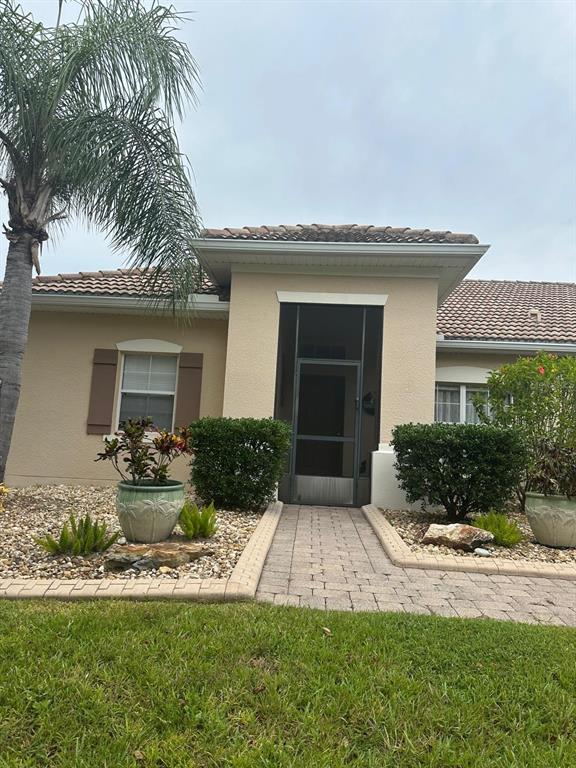 A beige stucco house features a tiled roof, a screened entryway, and a paver walkway — 4002 BOUGAINVILLEA PLACE, KISSIMMEE, FL