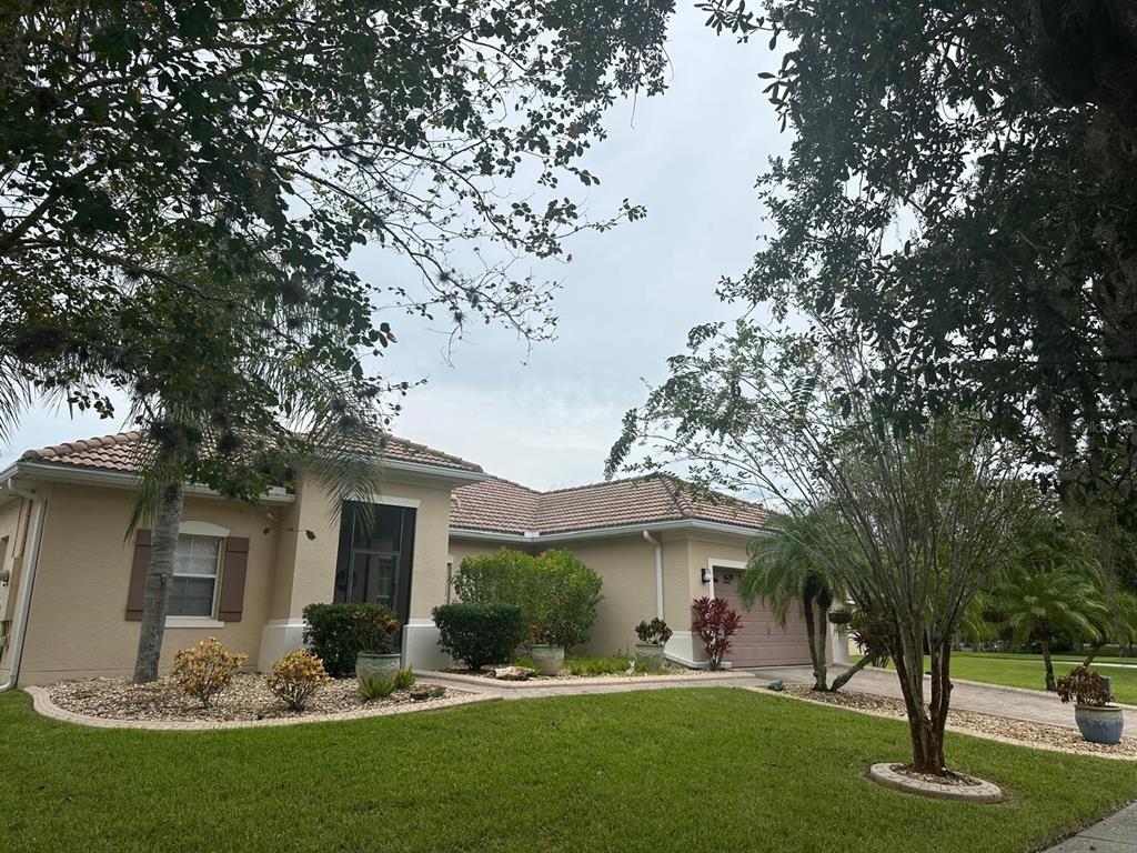A single-story beige house with a tiled roof, a two-car garage, and landscaped front yard — 4002 BOUGAINVILLEA PLACE, KISSIMMEE, FL