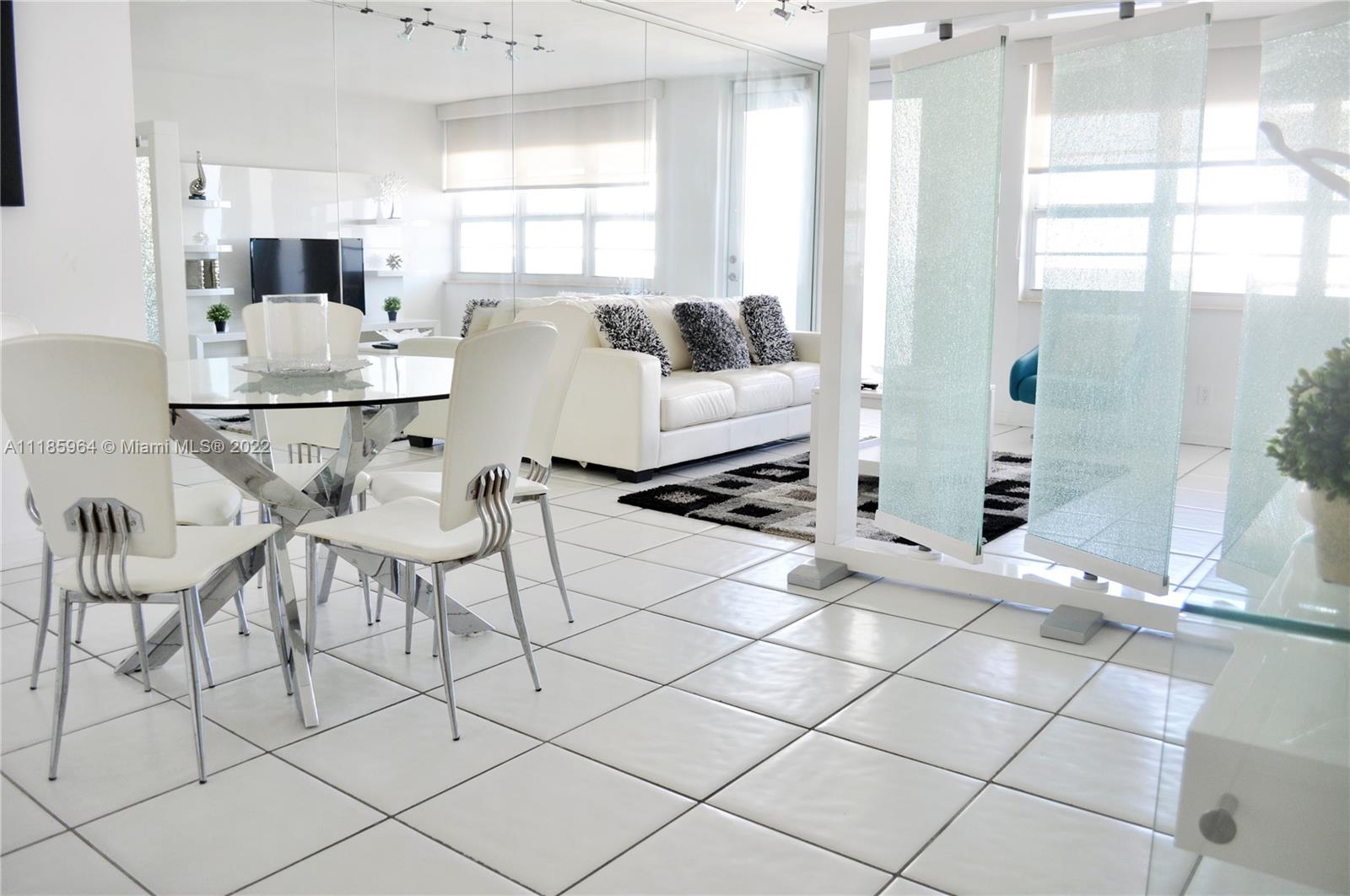 A dining area with a glass table and white chairs sits before a living room — 100 Lincoln Rd # 910, Miami Beach FL 33139, MIAMI BEACH, FL