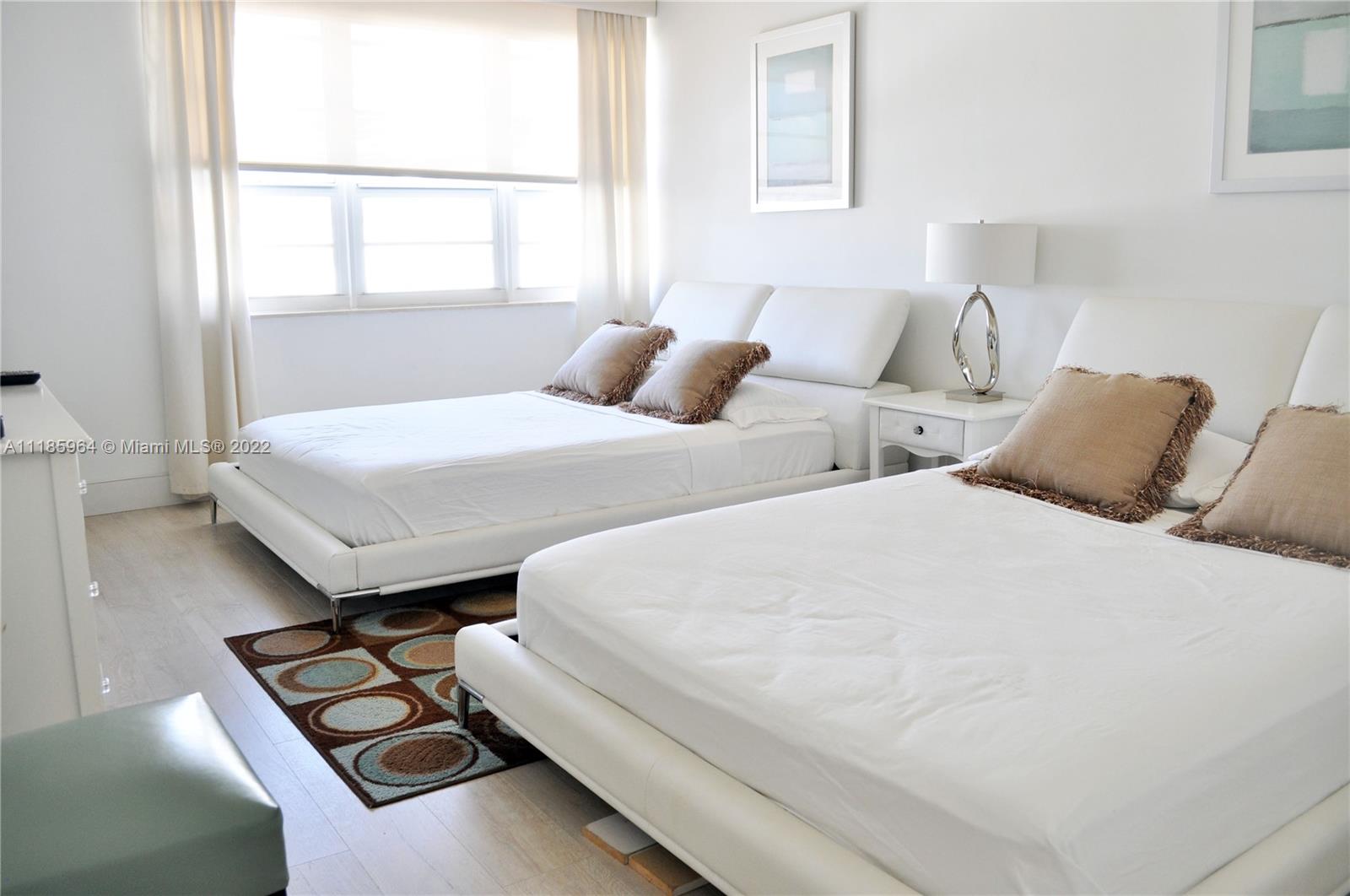 A bedroom features two white platform beds, a nightstand, and a patterned area rug — 100 Lincoln Rd # 910, Miami Beach FL 33139, MIAMI BEACH, FL