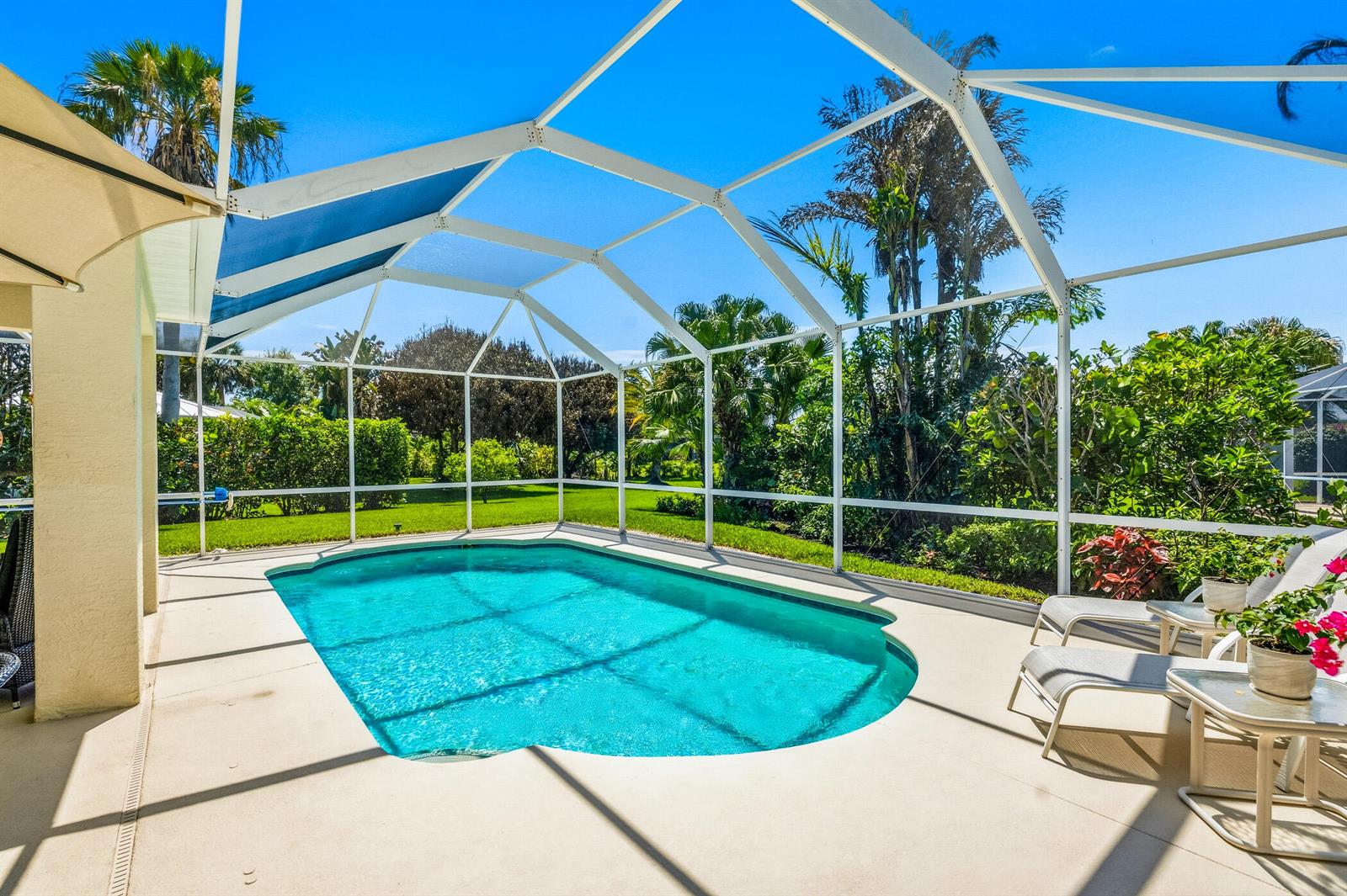 A screened-in swimming pool patio features lounge chairs and lush tropical landscaping in the background — 6455 36th Lane, Vero Beach FL 32966, VERO BEACH, FL