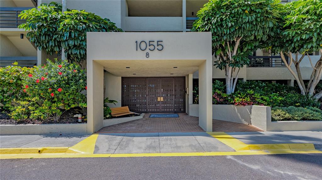 The exterior entrance of a multi-story building features a covered walkway with a wooden bench — 1055 GULF OF MEXICO DRIVE UNIT 504, LONGBOAT KEY, FL