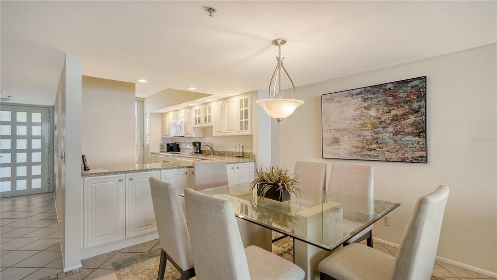 A dining area with a glass table and chairs sits adjacent to a white kitchen — 1055 GULF OF MEXICO DRIVE UNIT 504, LONGBOAT KEY, FL
