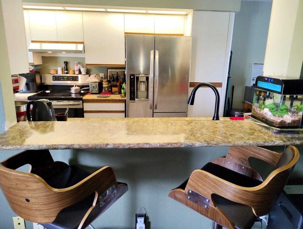 A kitchen features a breakfast bar with two wooden stools, stainless steel appliances, and cabinets — 3549 INDIGO POND DRIVE UNIT 2, PALM HARBOR, FL