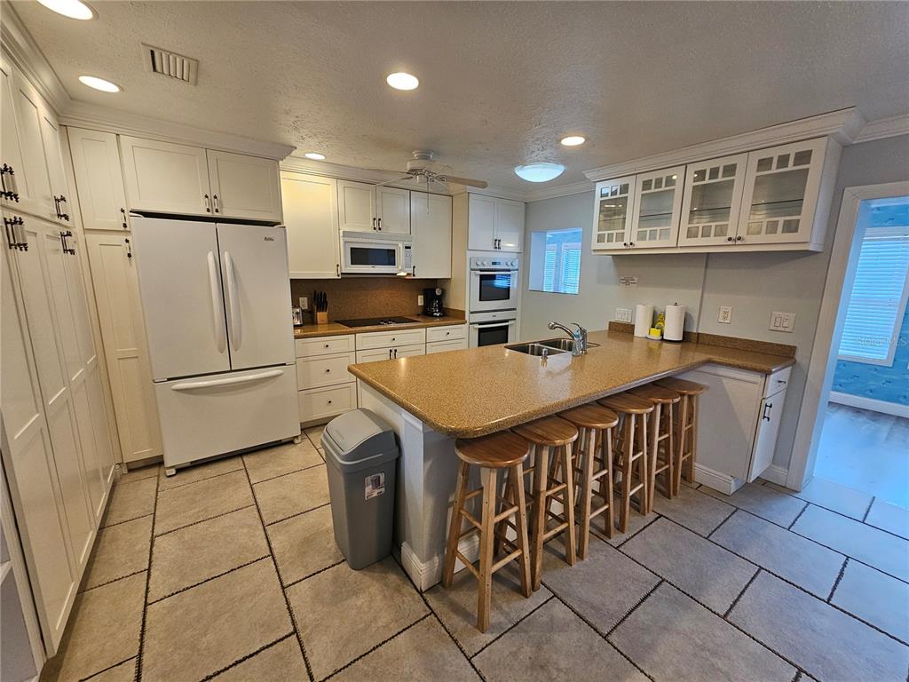 A kitchen features white cabinets, a tan countertop island with bar stools, and tiled flooring — 2130 PINEHURST STREET, SARASOTA, FL