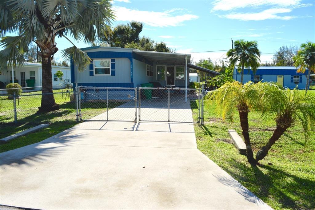 A blue mobile home with a concrete driveway and chain-link fence under a sunny sky — 15266 CIRCLE DRIVE, PUNTA GORDA, FL