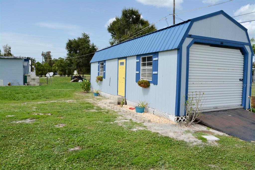 A light blue shed with a yellow door and a metal roll-up garage door — 15266 CIRCLE DRIVE, PUNTA GORDA, FL