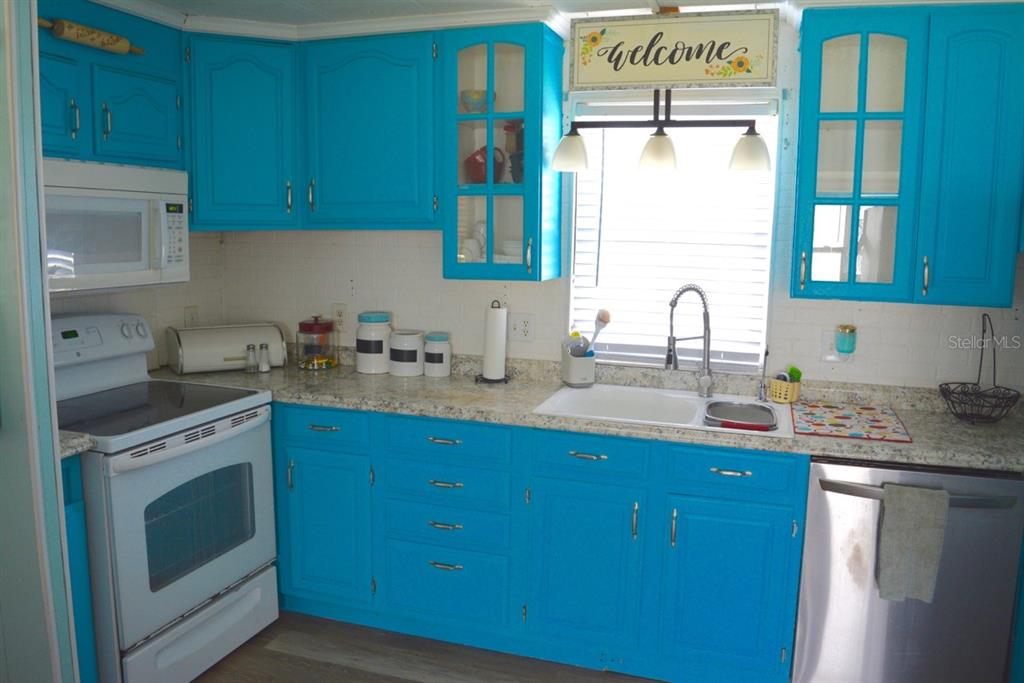 A kitchen features bright blue cabinets, white countertops, a white stove, and a stainless dishwasher — 15266 CIRCLE DRIVE, PUNTA GORDA, FL