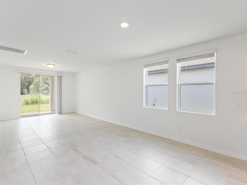 A bright, empty living room features white walls, light-colored tile flooring, two windows, and a sliding glass door — 4530 EAGLE PERCH COURT, ST CLOUD, FL