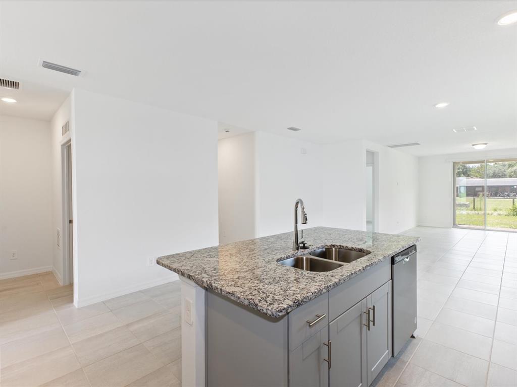 A kitchen island with a granite countertop and gray cabinets sits in an open room — 4530 EAGLE PERCH COURT, ST CLOUD, FL
