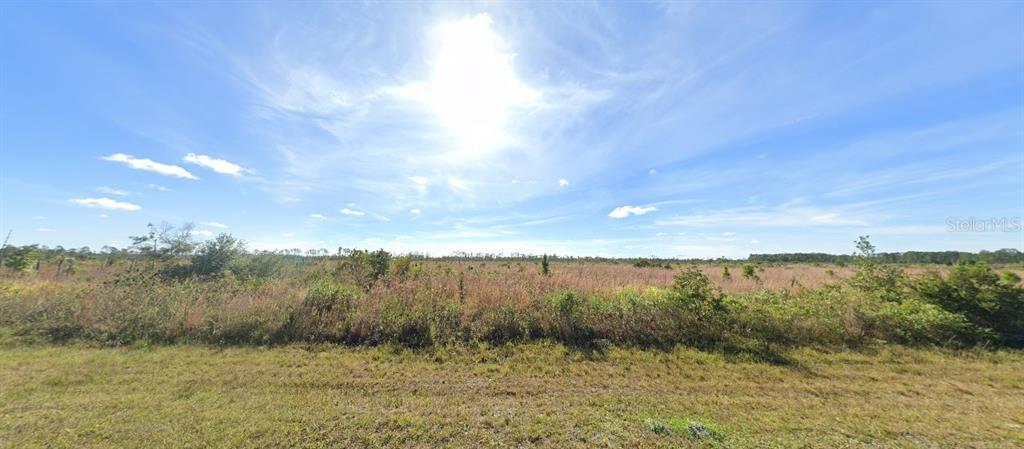 A wide, flat, grassy field under a bright blue sky with scattered clouds — 611 PORTULACA DRIVE, INDIAN LAKE ESTATES, FL