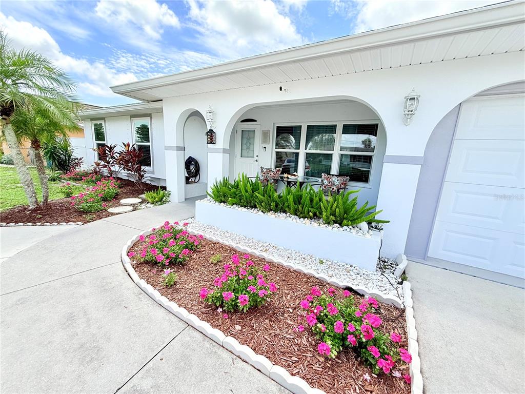 A white house exterior features a front porch, a raised planter, and a landscaped garden — 8509 LA BOCA AVENUE, NORTH PORT, FL