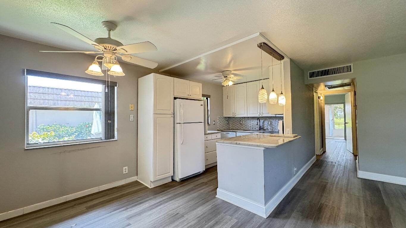 A kitchen with white cabinets, a white refrigerator, and a breakfast bar with pendant lights — 220 Seville J, Delray Beach FL 33446, DELRAY BEACH, FL