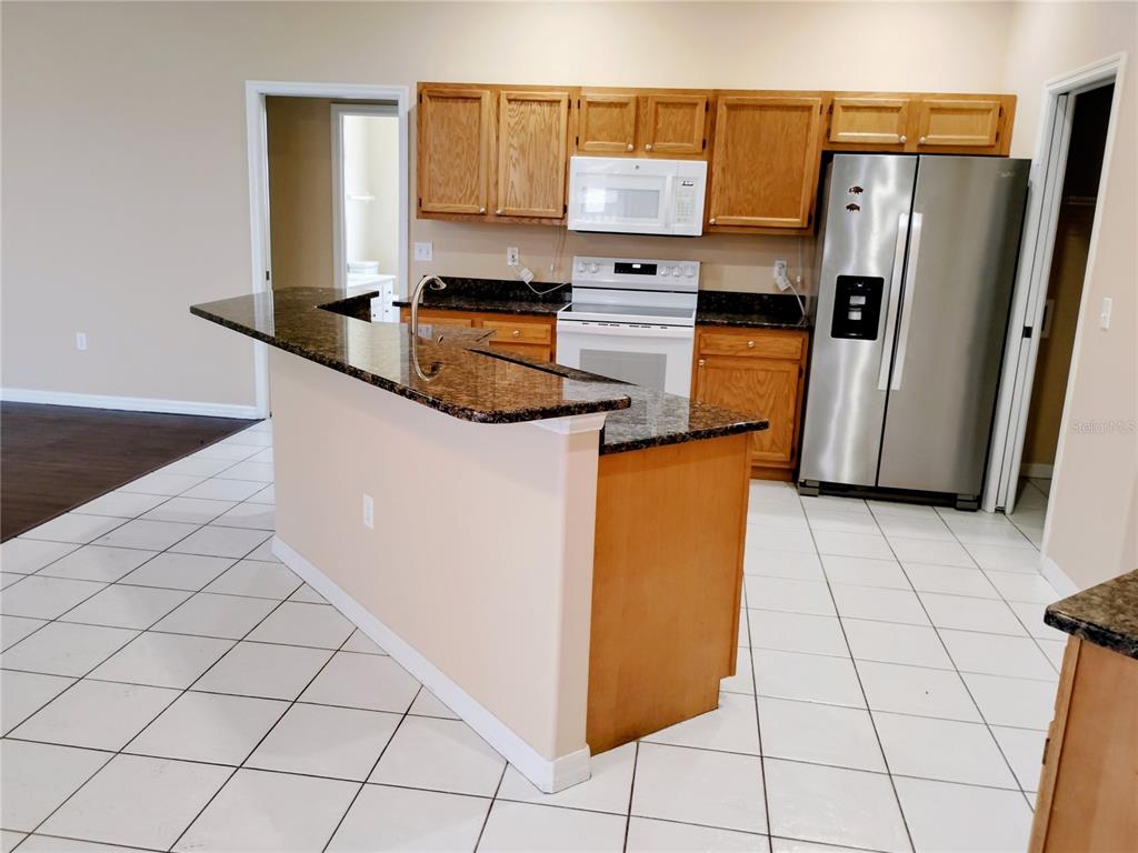 A kitchen features light wood cabinets, dark granite countertops, white appliances, and tiled flooring — 4509 30TH LANE E, BRADENTON, FL