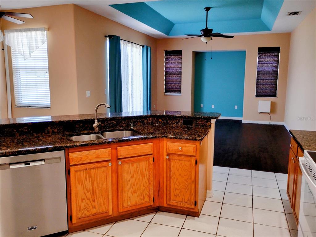 A kitchen with granite countertops and wood cabinets overlooks a living area with blue accents — 4509 30TH LANE E, BRADENTON, FL