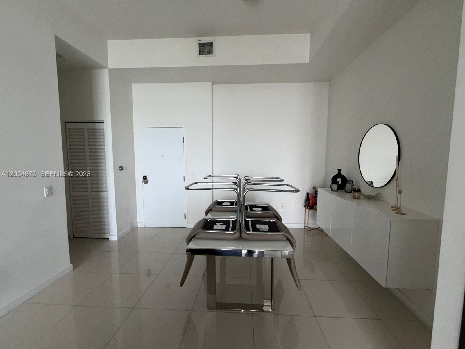 A dining room features a white console table, a round mirror, and chairs stacked on a table — 7825 NW 107th Ave # 818, Doral FL 33178, DORAL, FL