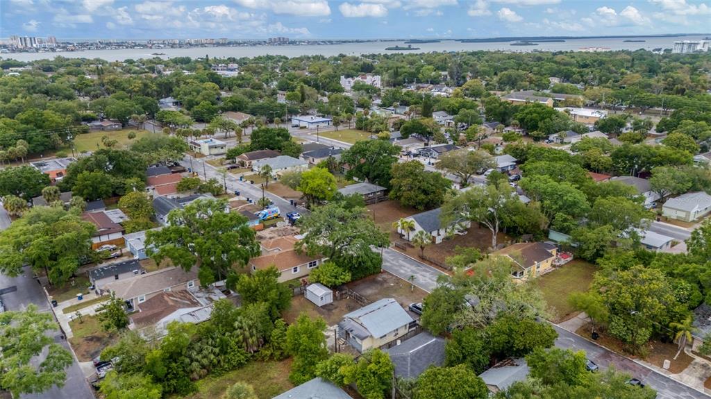 An aerial view shows a residential neighborhood with houses, trees, and a distant body of water — 1127 ENGMAN STREET, CLEARWATER, FL