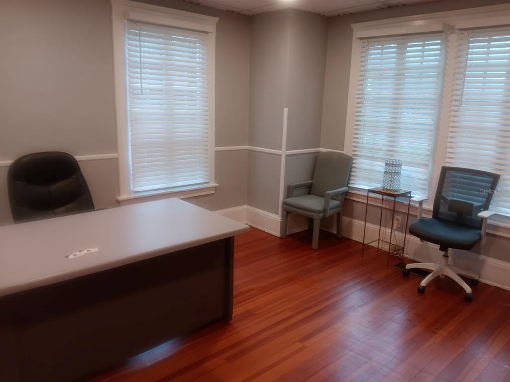 An office room features a desk, two chairs, hardwood floors, and windows with white blinds — 457 S RIDGEWOOD AVENUE UNIT E, DAYTONA BEACH, FL