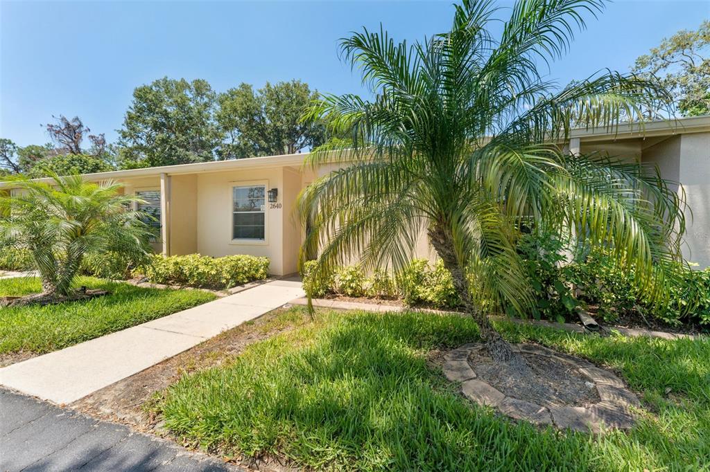 The exterior of a single-story home features a concrete walkway, palm trees, and landscaping — 2640 WOODGATE LANE UNIT F6, SARASOTA, FL