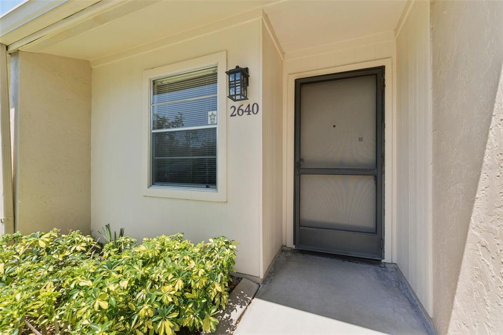A beige exterior wall features a window, a house number, and a screen door — 2640 WOODGATE LANE UNIT F6, SARASOTA, FL