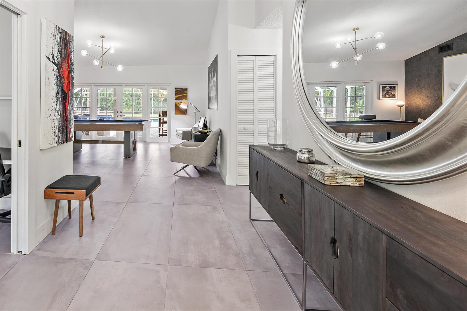 A modern entryway with a large circular mirror, dark wood console, and a pool table beyond — 14039 Greentree Trail, Wellington FL 33414, WELLINGTON, FL