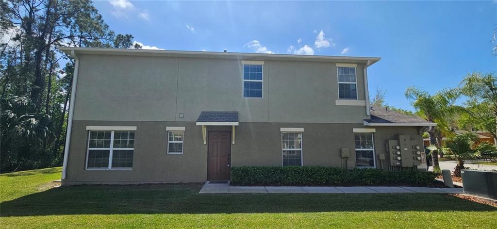 A two-story building exterior features a brown door, multiple windows, and a grassy lawn — 2802 BIRCHCREEK DRIVE, WESLEY CHAPEL, FL