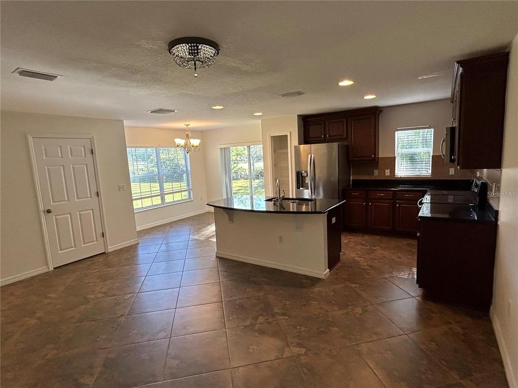 A kitchen with dark wood cabinets, black countertops, and tile flooring opens to a dining area — 2802 BIRCHCREEK DRIVE, WESLEY CHAPEL, FL