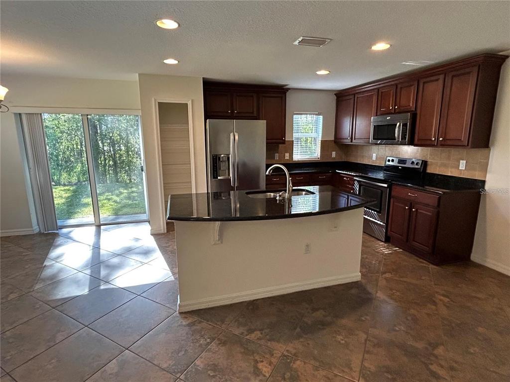A kitchen features dark wood cabinets, black granite countertops, a center island, and tile flooring — 2802 BIRCHCREEK DRIVE, WESLEY CHAPEL, FL