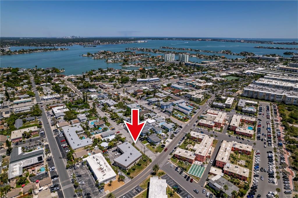 An aerial view shows a low-rise building marked by a red arrow in a coastal neighborhood — 7003 SUNSET WAY UNIT 3, ST PETE BEACH, FL