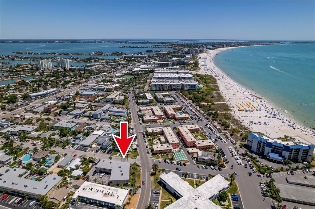 An aerial view shows a coastal town with a red arrow pointing toward a building — 7003 SUNSET WAY UNIT 3, ST PETE BEACH, FL