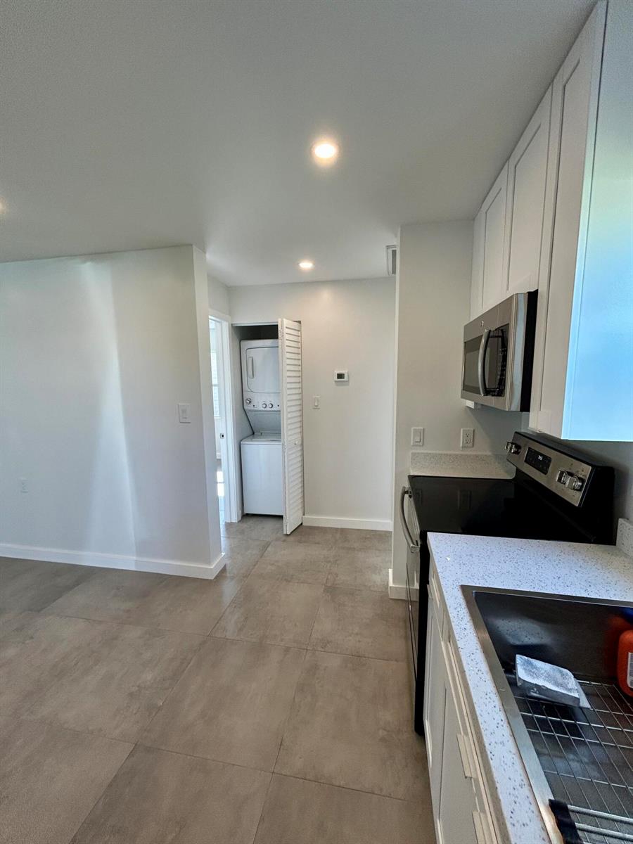 A kitchen with white cabinets and grey tile flooring features a stacked laundry unit nearby — 1134 6th Street, Okeechobee FL 34974, OKEECHOBEE, FL
