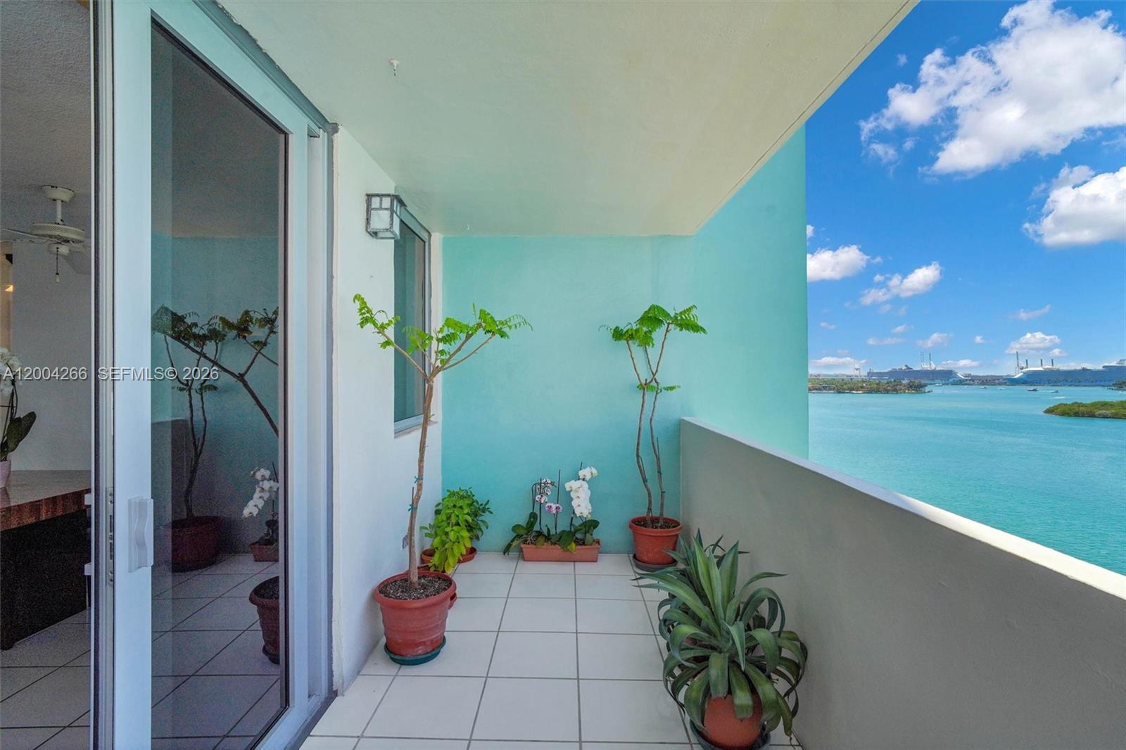 A balcony with potted plants overlooks a blue bay with cruise ships in the distance — 5 Island Ave # 12C, Miami Beach FL 33139, MIAMI BEACH, FL