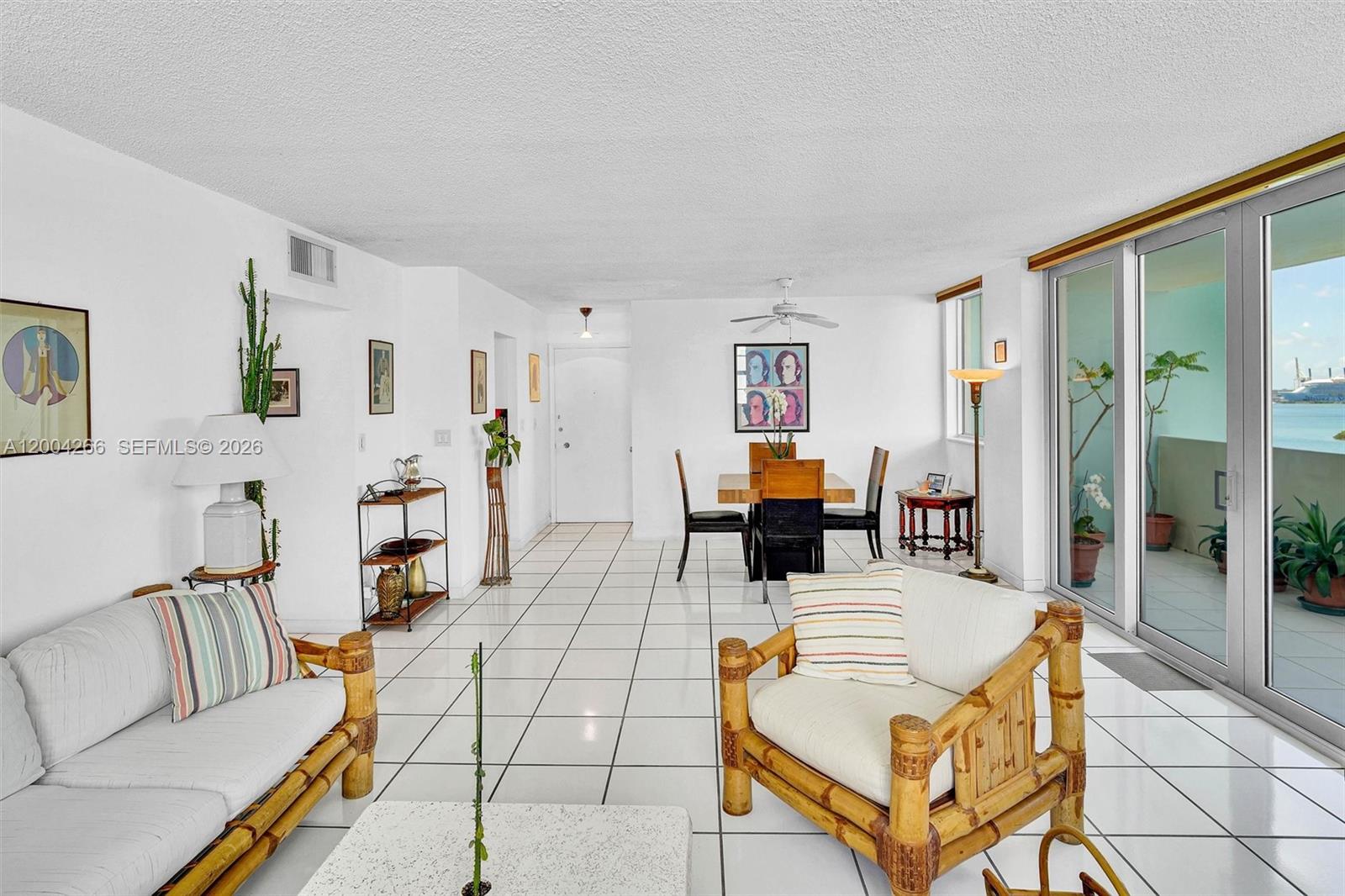 A living and dining area features white tiled floors, bamboo furniture, and a balcony view — 5 Island Ave # 12C, Miami Beach FL 33139, MIAMI BEACH, FL
