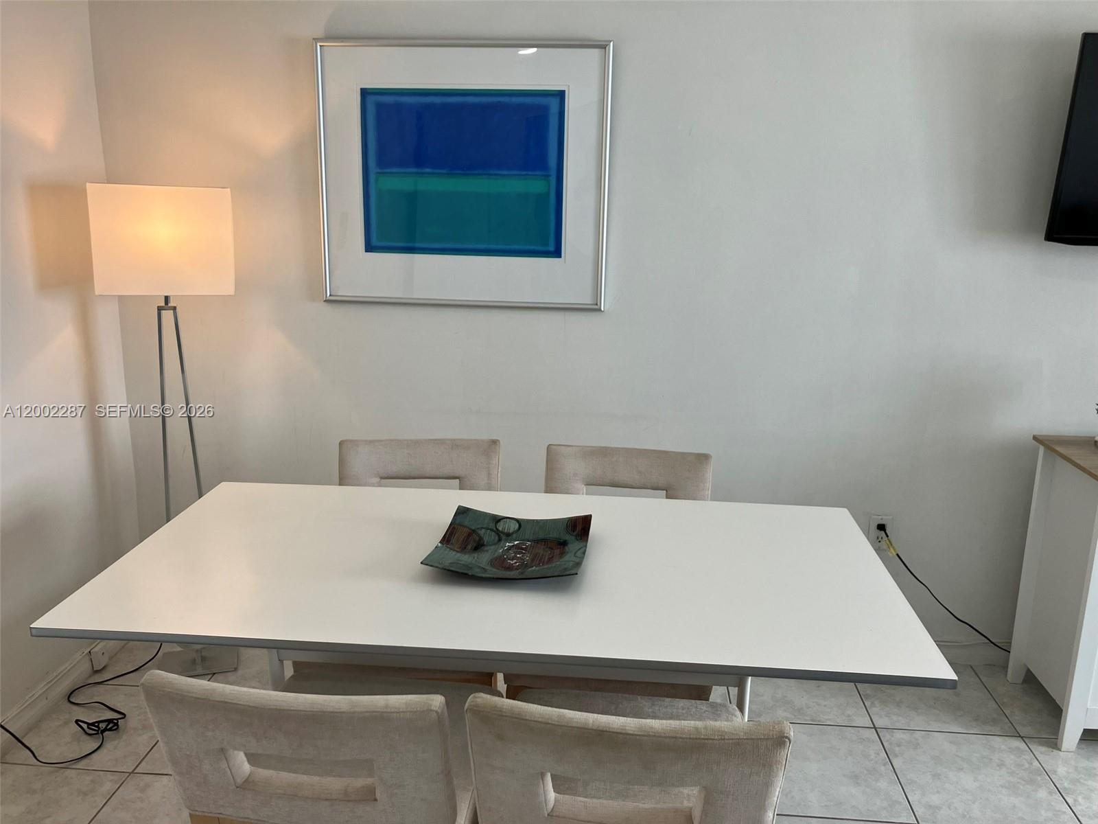 A dining room features a white table, four upholstered chairs, and a framed abstract painting — 335 Ocean Dr # 306, Miami Beach FL 33139, MIAMI BEACH, FL