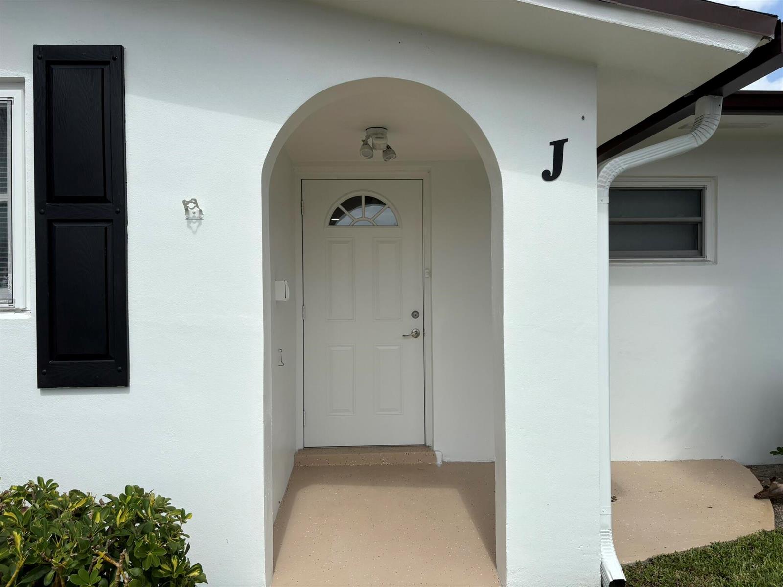 The exterior of a white home features a black shutter, arched entryway, and letter J — 2930 CROSLEY Drive E # J, West Palm Beach FL 33415, WEST PALM BEACH, FL