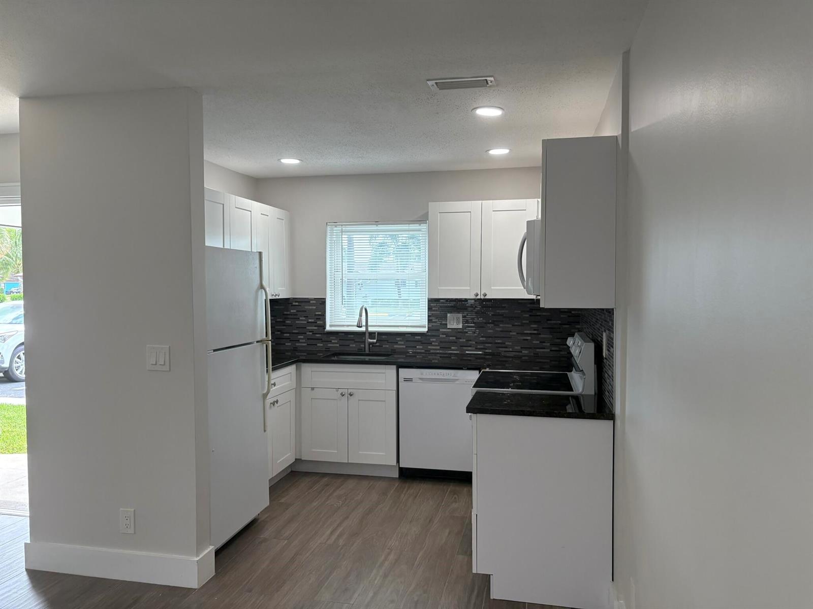 A kitchen features white cabinets, dark countertops, a tiled backsplash, and stainless steel appliances — 2930 CROSLEY Drive E # J, West Palm Beach FL 33415, WEST PALM BEACH, FL